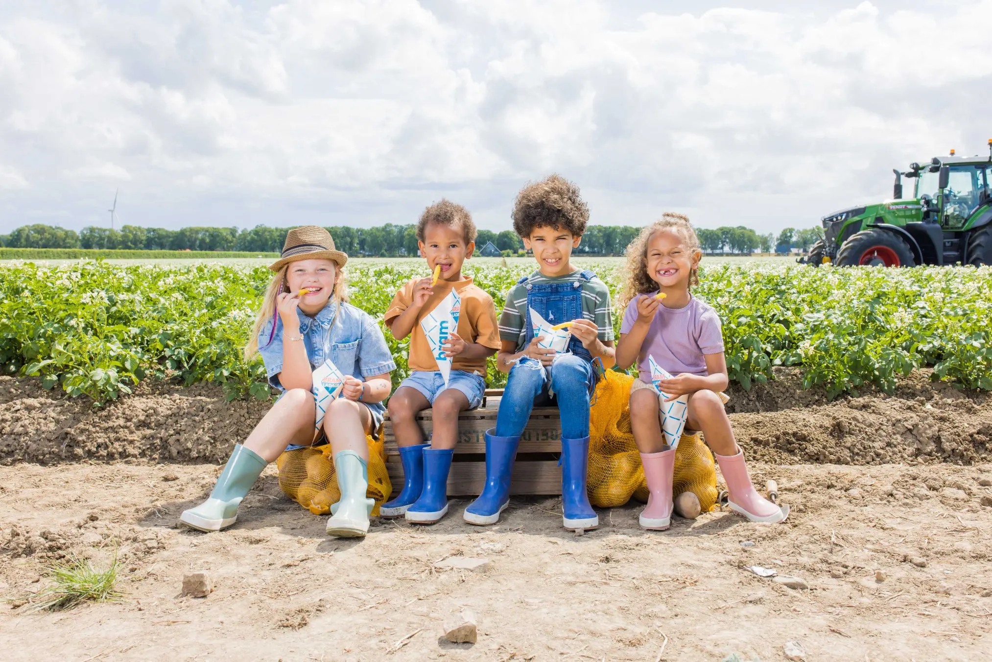 vier kinderen die een brammetje eten op het aardappelveld