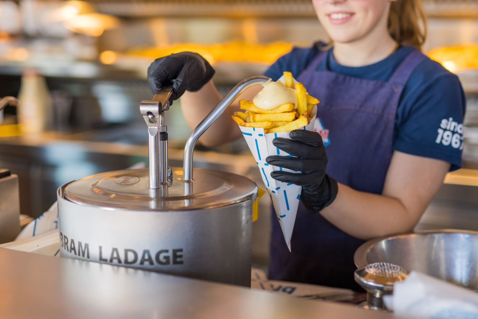 medewerker die met de pomp fritessaus op de puntzak doet